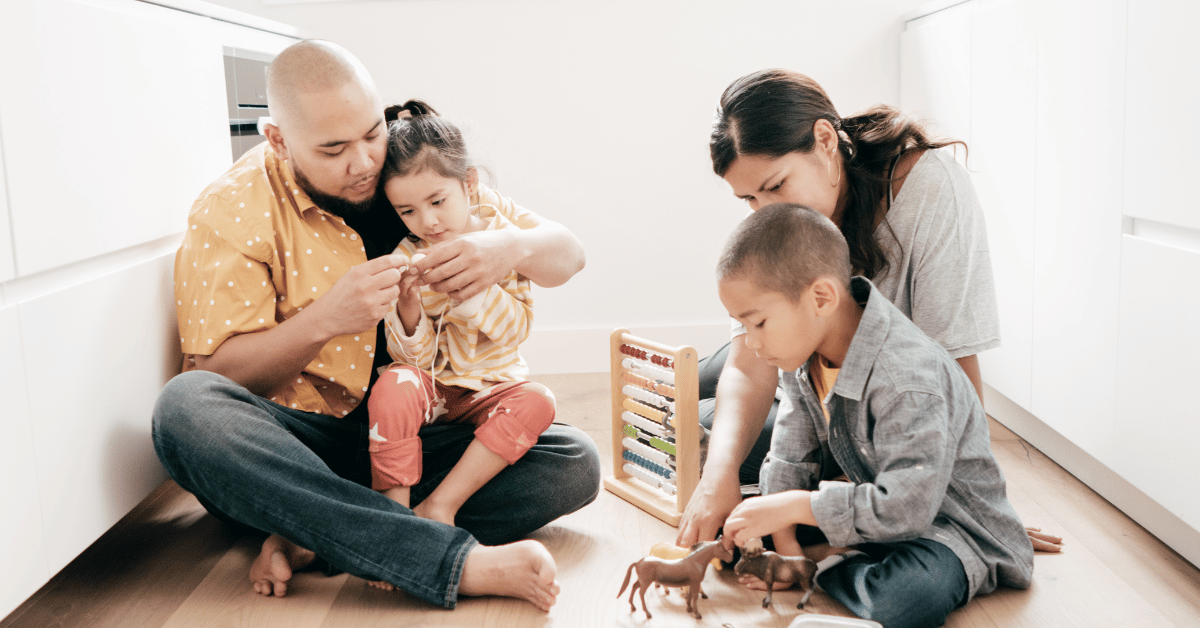 Two young parents playing with son and daughter on floor