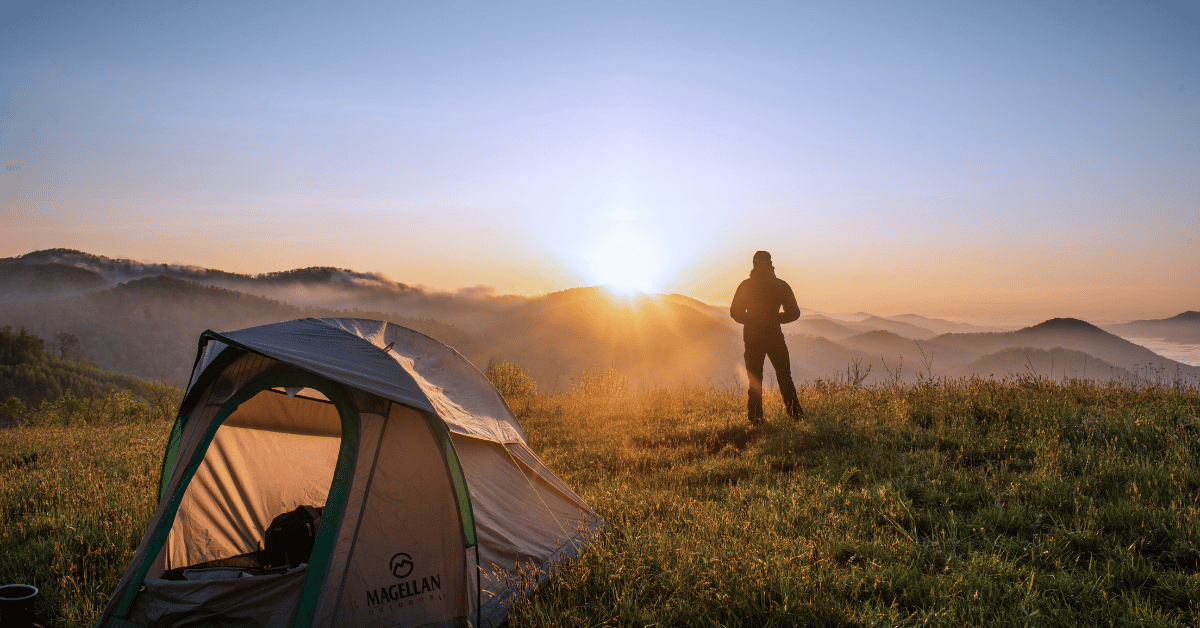 Person standing outside tent at sunrise in the hills